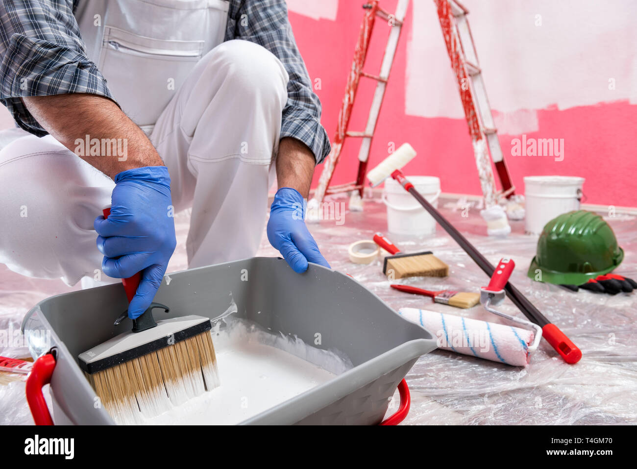 Kaukasische Haus Maler Arbeiter in weißen Overalls, bereiten die weiße Farbe die rosa Wand zu malen. Bauindustrie. Arbeitssicherheit. Stockfoto