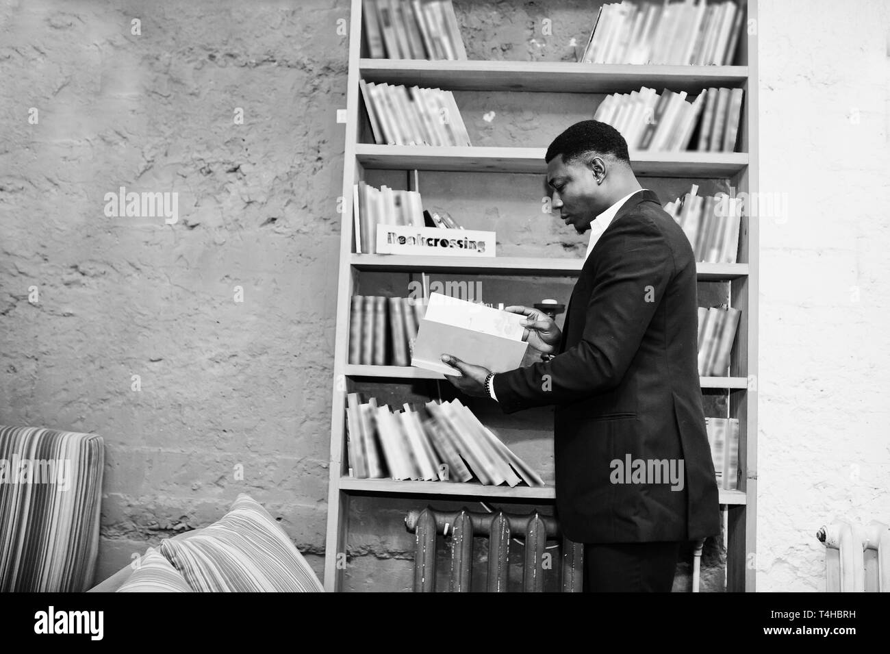 Starke mächtige afrikanische amerikanische Mann im schwarzen Anzug Buch lesen gegen Regale in freie Bücher anti Cafe. Stockfoto