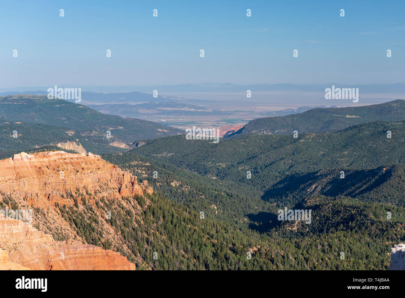 Orange karge Berggipfel mit grün bewaldeten Berge und das Tal unten, dunstig blauen Himmel. Stockfoto