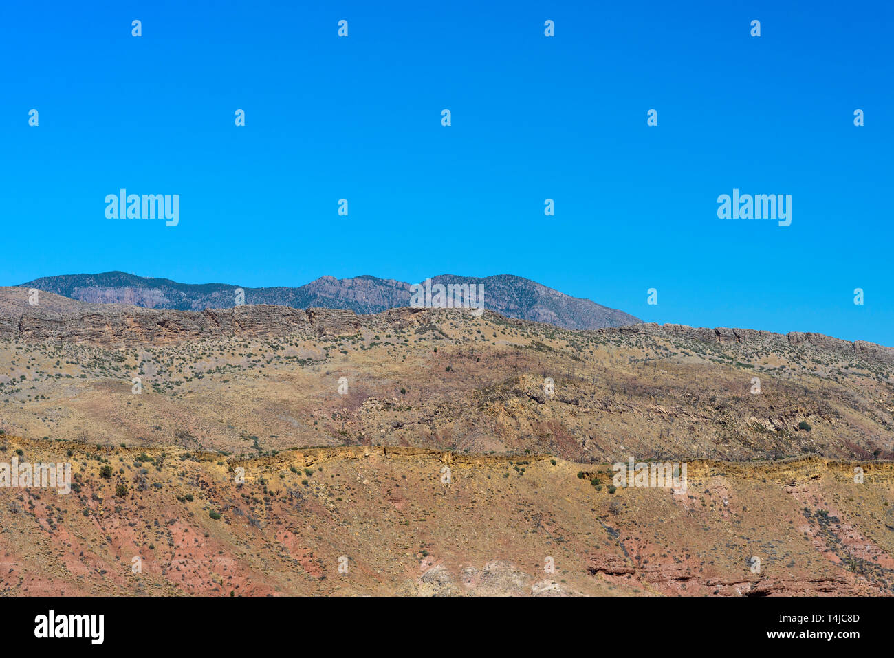 Gelb rote Wüste Berge mit spärlicher Vegetation unter einem strahlend blauen Himmel. Stockfoto
