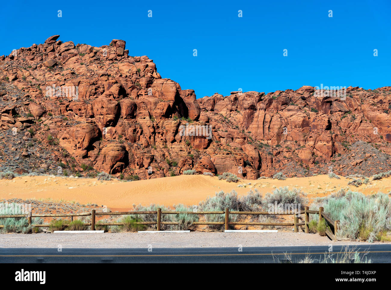 Anmelden Zaun mit Salbei Pinsel gibt Weg für gelbe Wüste Sand Dünen mit karge raue Red Rock Mountain unter einem strahlend blauen Himmel. Stockfoto