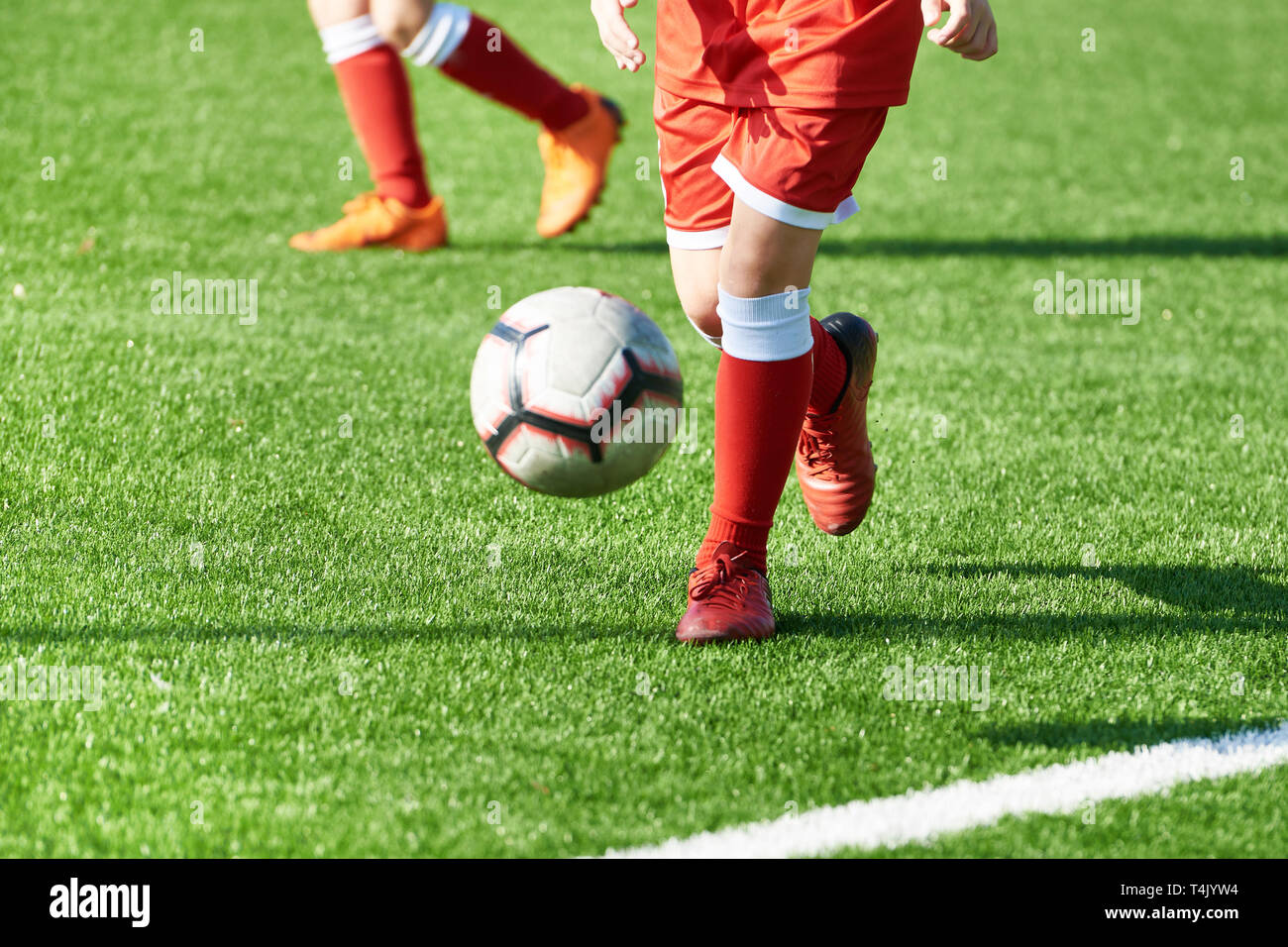 Beine eines Fußball-Jungen in roten Sport einheitliche mit einer Kugel auf einem Fußball Feld Stockfoto