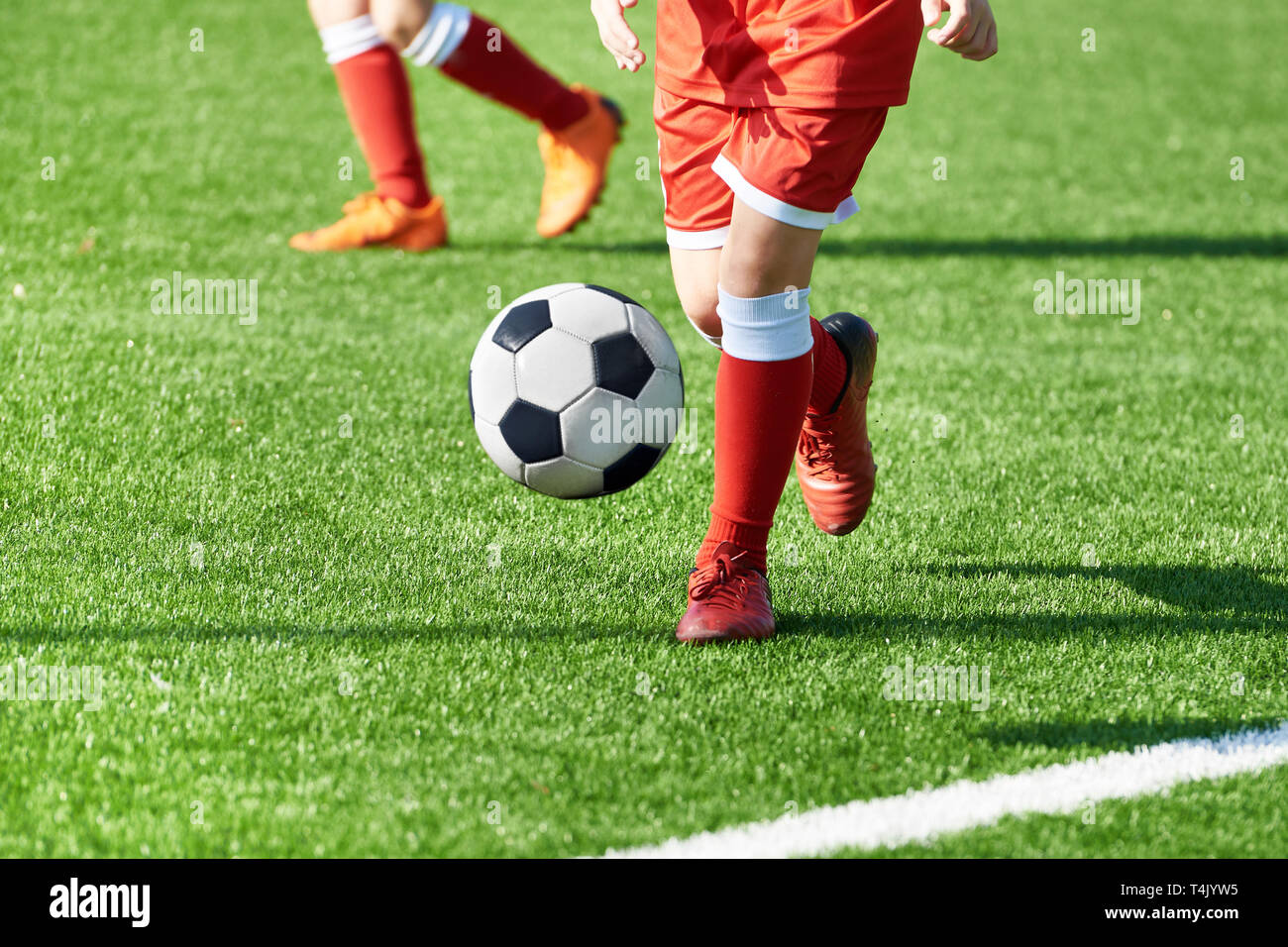 Beine eines Fußball-Jungen in roten Sport einheitliche mit einer Kugel auf einem Fußball Feld Stockfoto