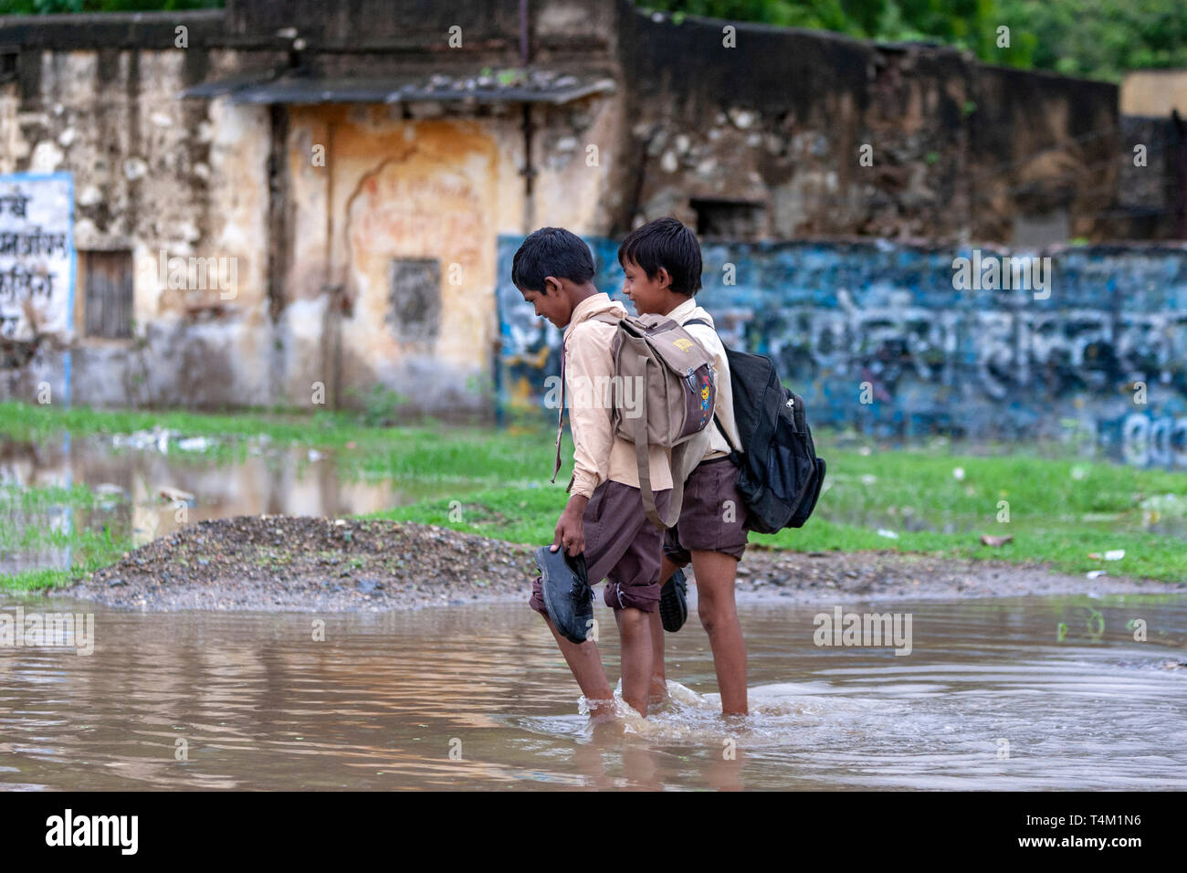 Zwei benetzt Studenten Boys in einer großen Pfütze während des Monsuns in Rajasthan, Indien Stockfoto