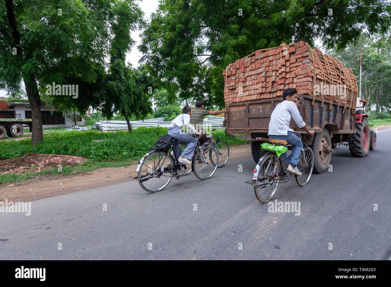 Jungen mit seinem Fahrrad mit einem Traktor voller Steine in Uttar Pradesh, Indien Stockfoto