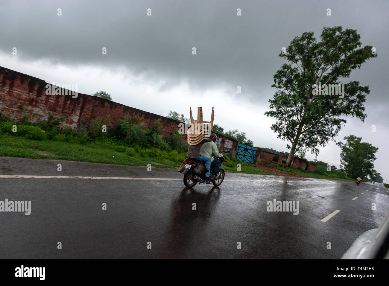 Motorrad mit einem Passagier die Plastik Stühlen unter einem schweren Regen, Uttar Pradesh, Indien Stockfoto