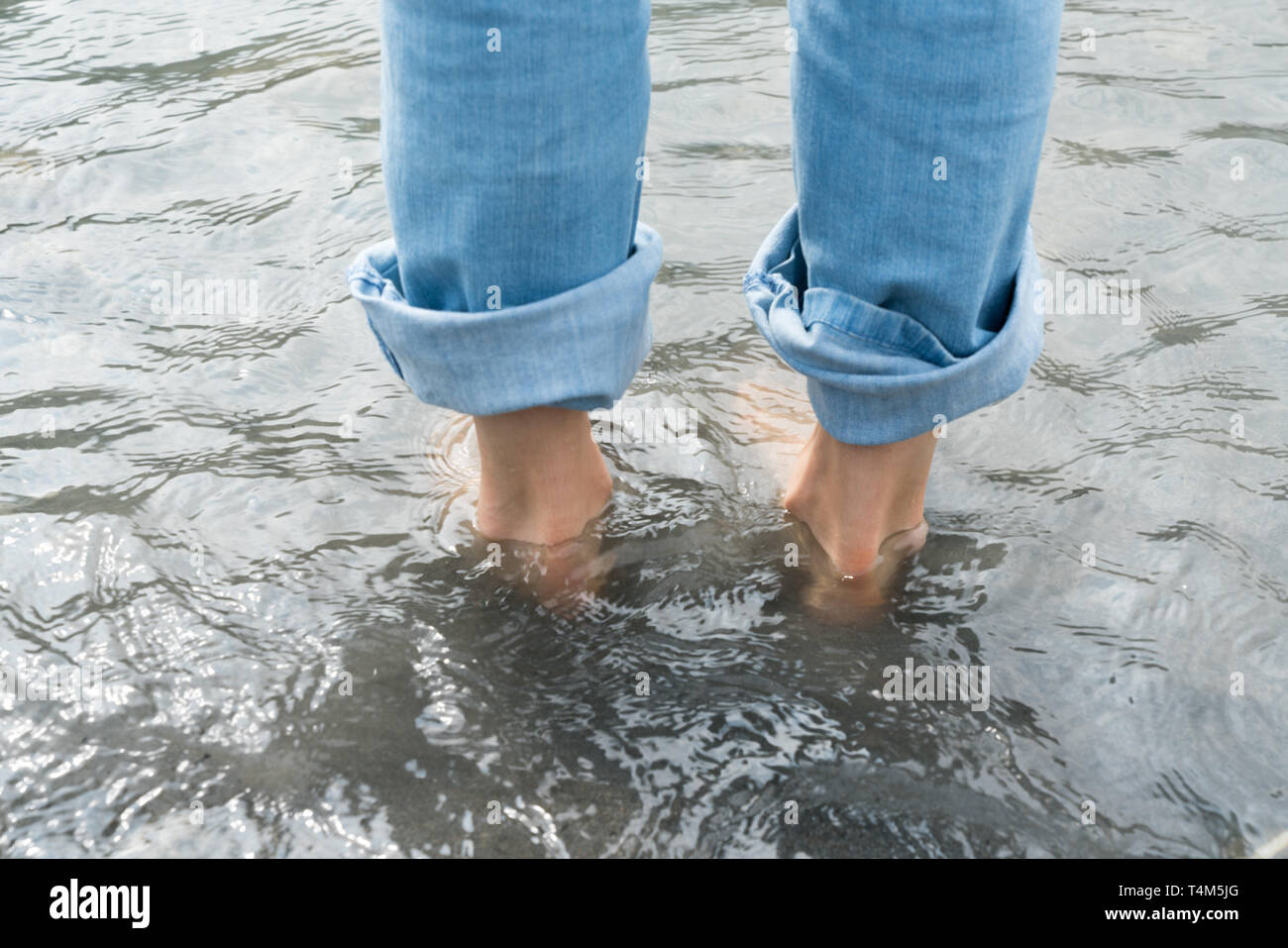 Füße der Frau trägt blaue Jeans in kaltem Wasser bei einem Kneipp-Fußbad Stockfoto