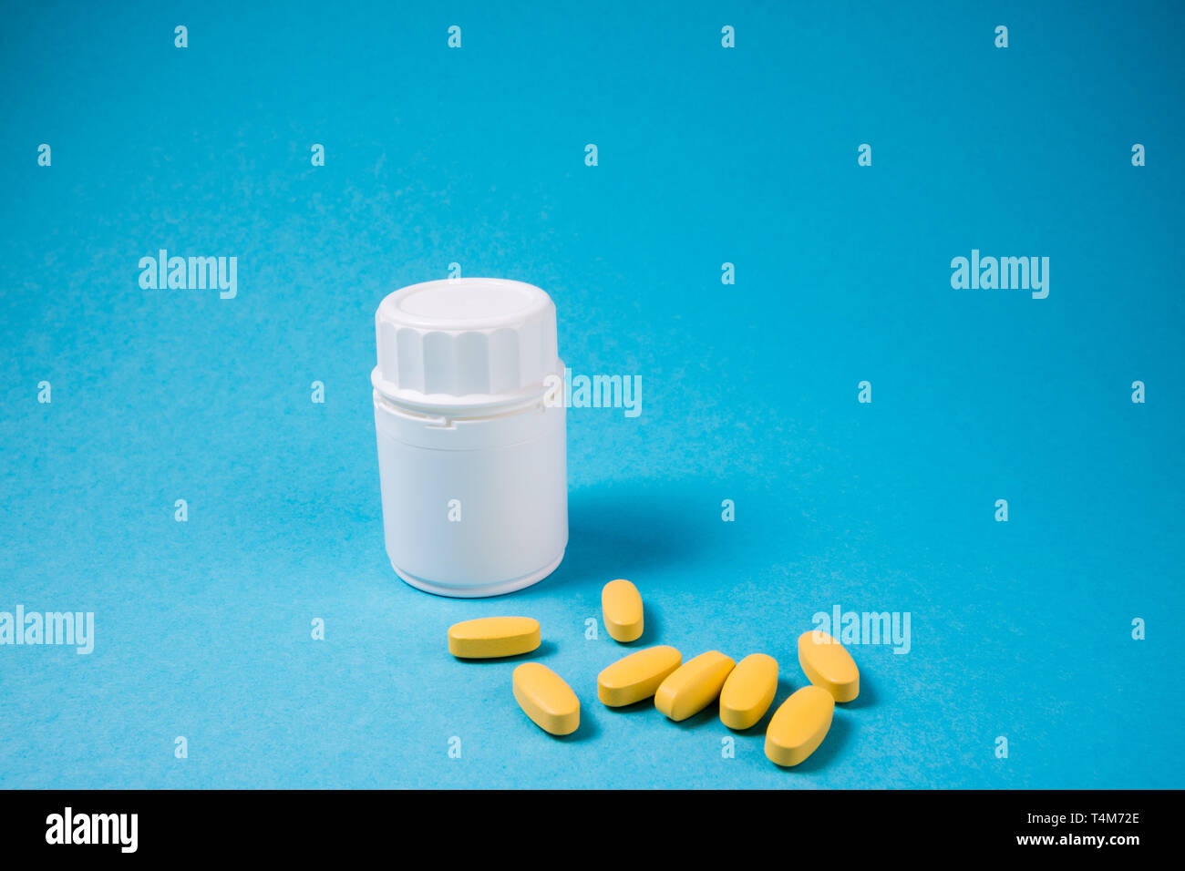 Weiße Flasche mit gelben Pillen Vitamine. Pharmazeutische medizinische Pillen, Tabletten auf blauem Hintergrund. Medizin Hintergrund mit Kopie Raum Stockfoto