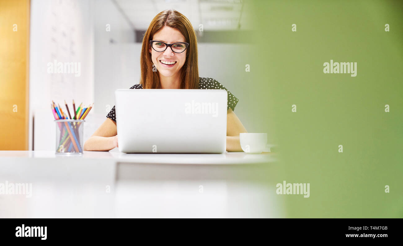 Junge Geschäftsfrau mit Laptop arbeitet In Co-Working Raum Stockfoto