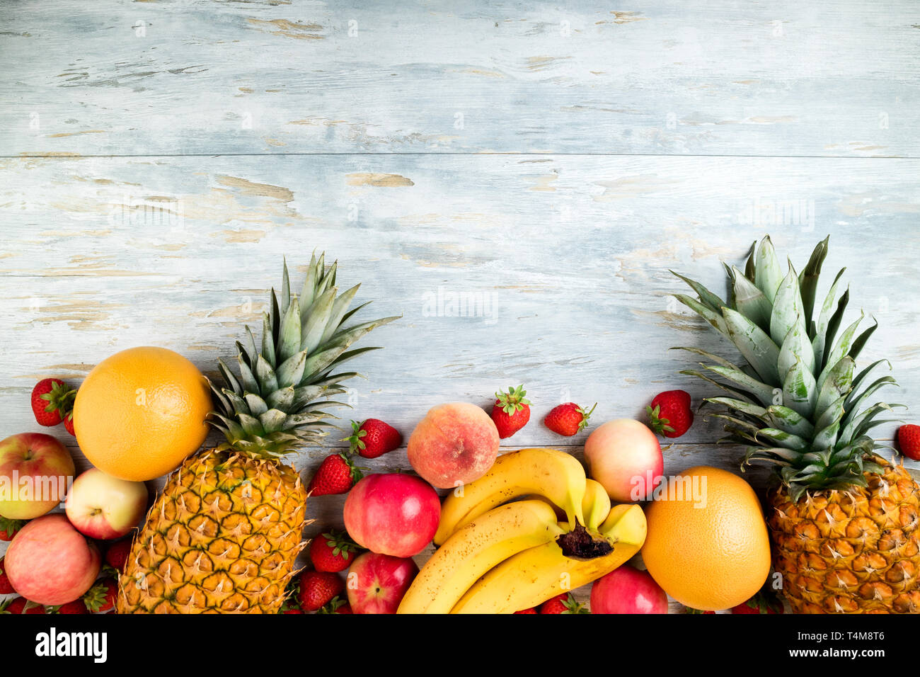 Vielzahl von Obst auf alten Holztisch. Ananas, Banane, Apfel, Berry, Zitrone und Pfirsich. Gesunde Lebensmittel sauber essen Auswahl. Ansicht von oben. Platz kopieren Stockfoto