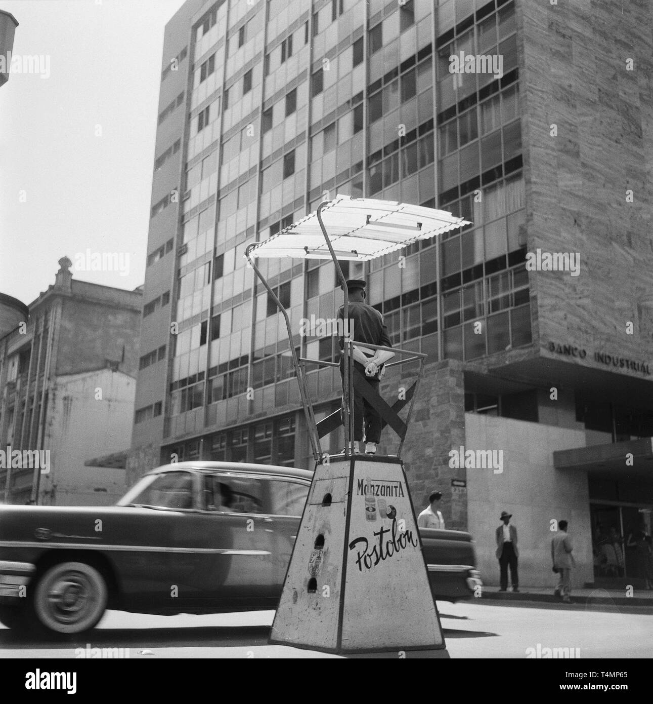 Verkehrspolizist in überdachten Kanzel, vor dem Hochhaus der Banco Industrial Colombiano in der Mitte der Stadt, Medellin (Antioquia), Kolumbien, 1958. | Verwendung weltweit Stockfoto