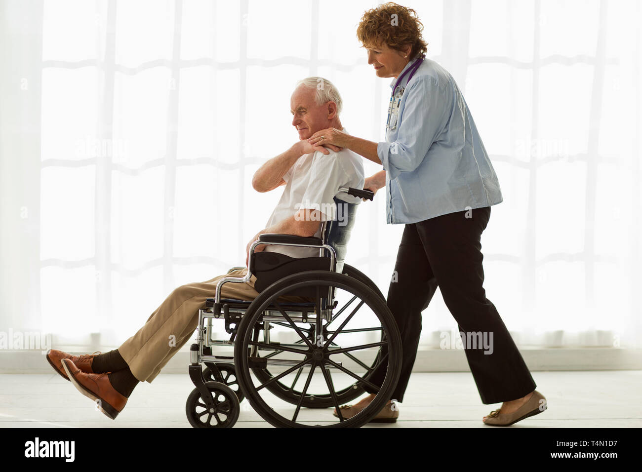 Reifen Arzt drückt einen älteren Patienten im Rollstuhl. Stockfoto