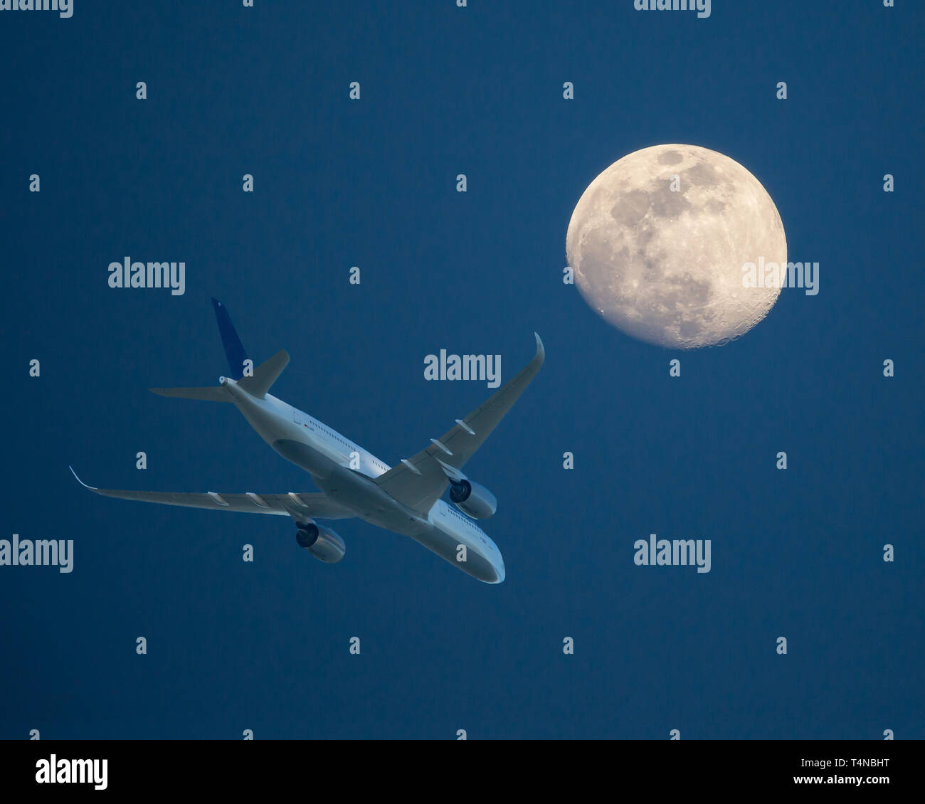 Ein Verkehrsflugzeug in niedriger Höhe passiert einen Vollmond bei Sonnenuntergang. Stockfoto