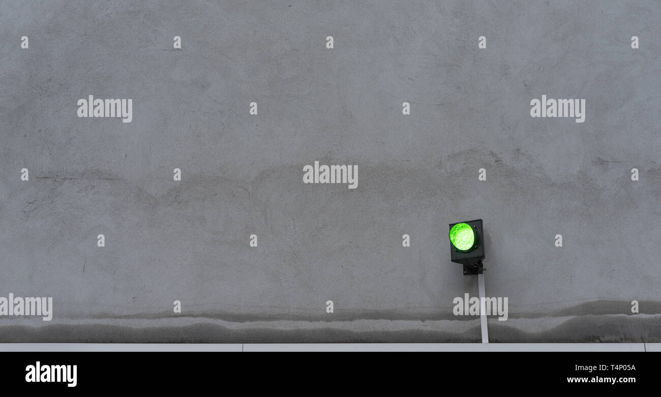 Die Ampel leuchtet grün vor der grauen Wand Stockfoto
