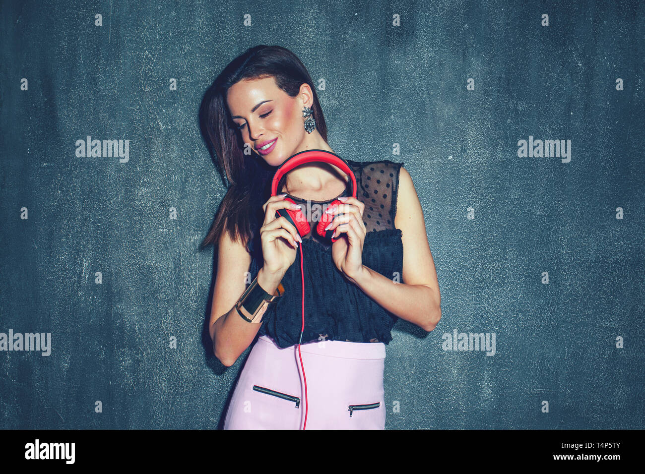 Stilvolle junge Frau mit Kopfhörern bei Wand nuancierte Stockfoto