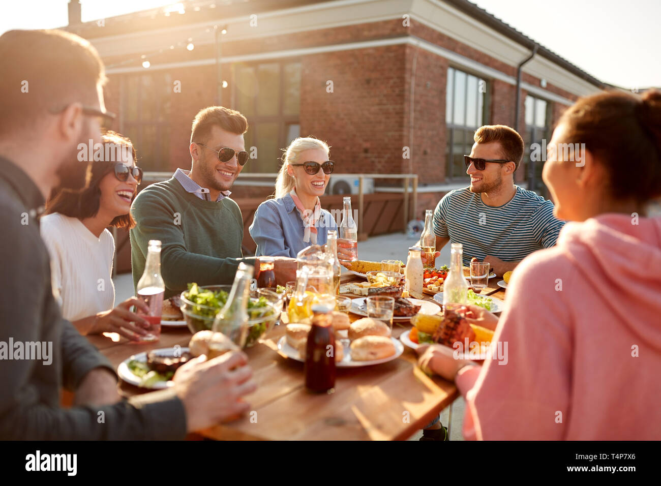 Freizeitaktivitäten und Personen Konzept - glückliche Freunde mit Getränke beim Abendessen oder Grillabend auf der Dachterrasse Stockfoto