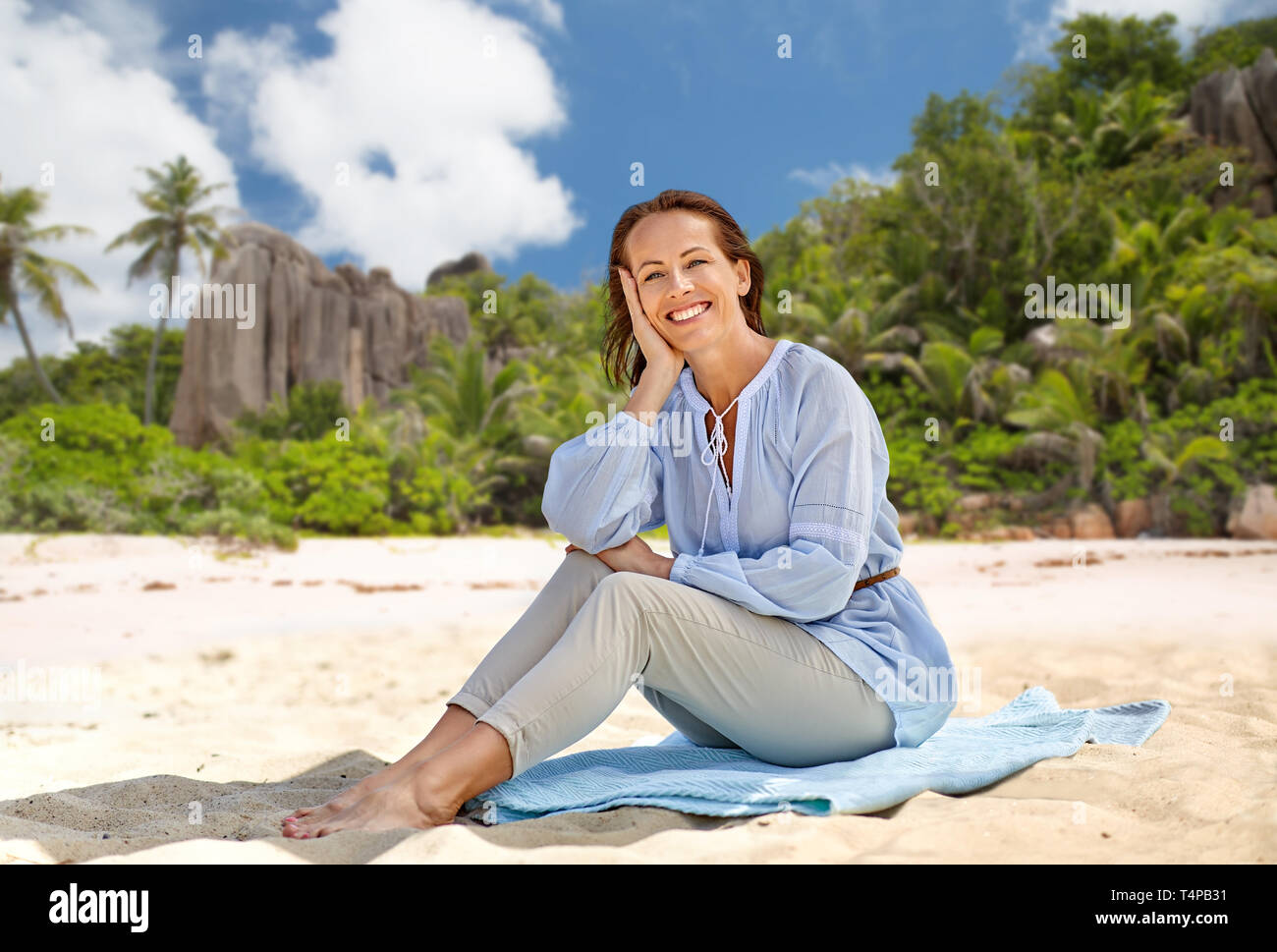 Menschen und Sommer Konzept - Glücklich lächelnde Frau sitzt auf dem Handtuch über Seychellen Insel tropischen Strand Hintergrund Stockfoto