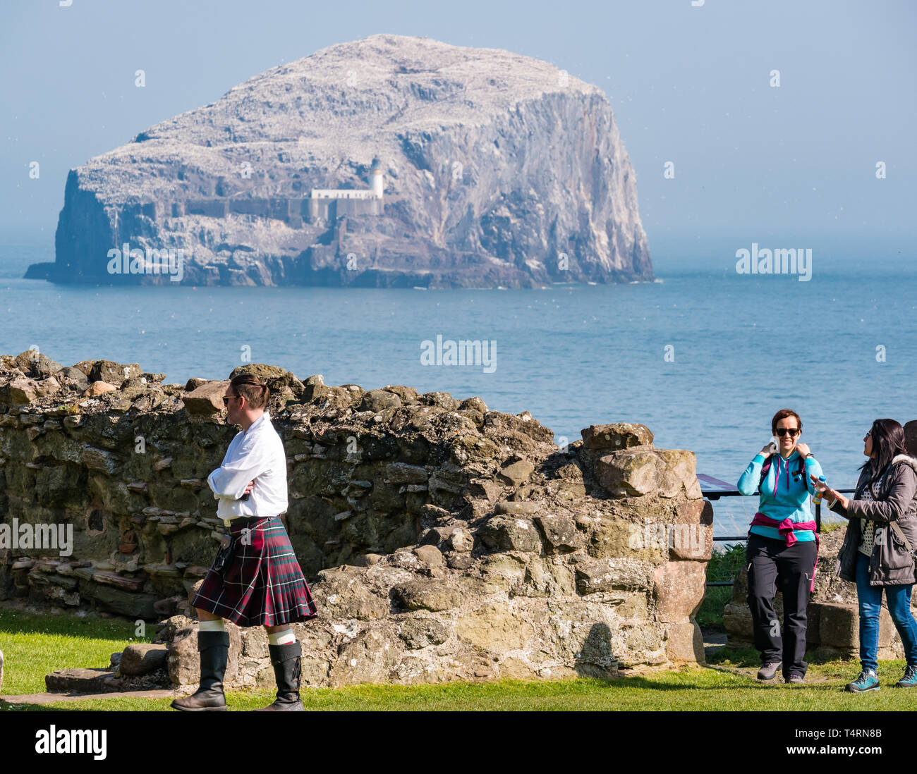 Tantallon Castle, North Berwick, East Lothian, Schottland, Vereinigtes Königreich, 19th. April 2019. Großbritannien Wetter: Historische Umgebung Schottlands zerstörte Burg aus dem 14th. Jahrhundert. Die Vorhangmauer Burg mit Blick auf die größte Nördliche Gannetkolonie auf dem Bass Rock im Firth of Forth. Die Tölpel vereinen sich wieder und bauen Nester. Ein Reiseführer mit einem Kilt zeigt zwei weibliche Touristen rund um das Schloss Stockfoto