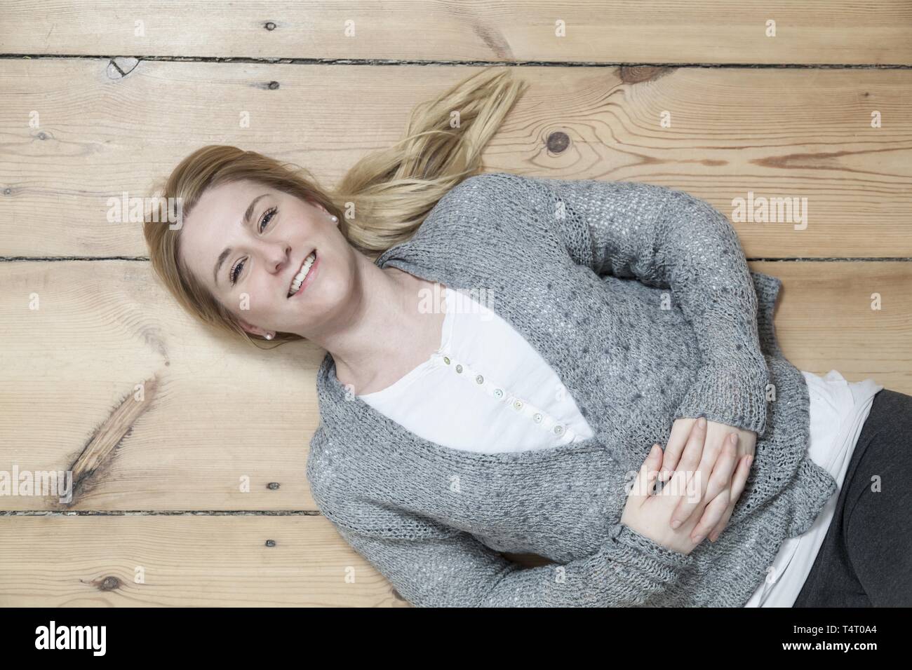 Junge blonde Frau liegend auf dem Holzboden, von oben Stockfoto