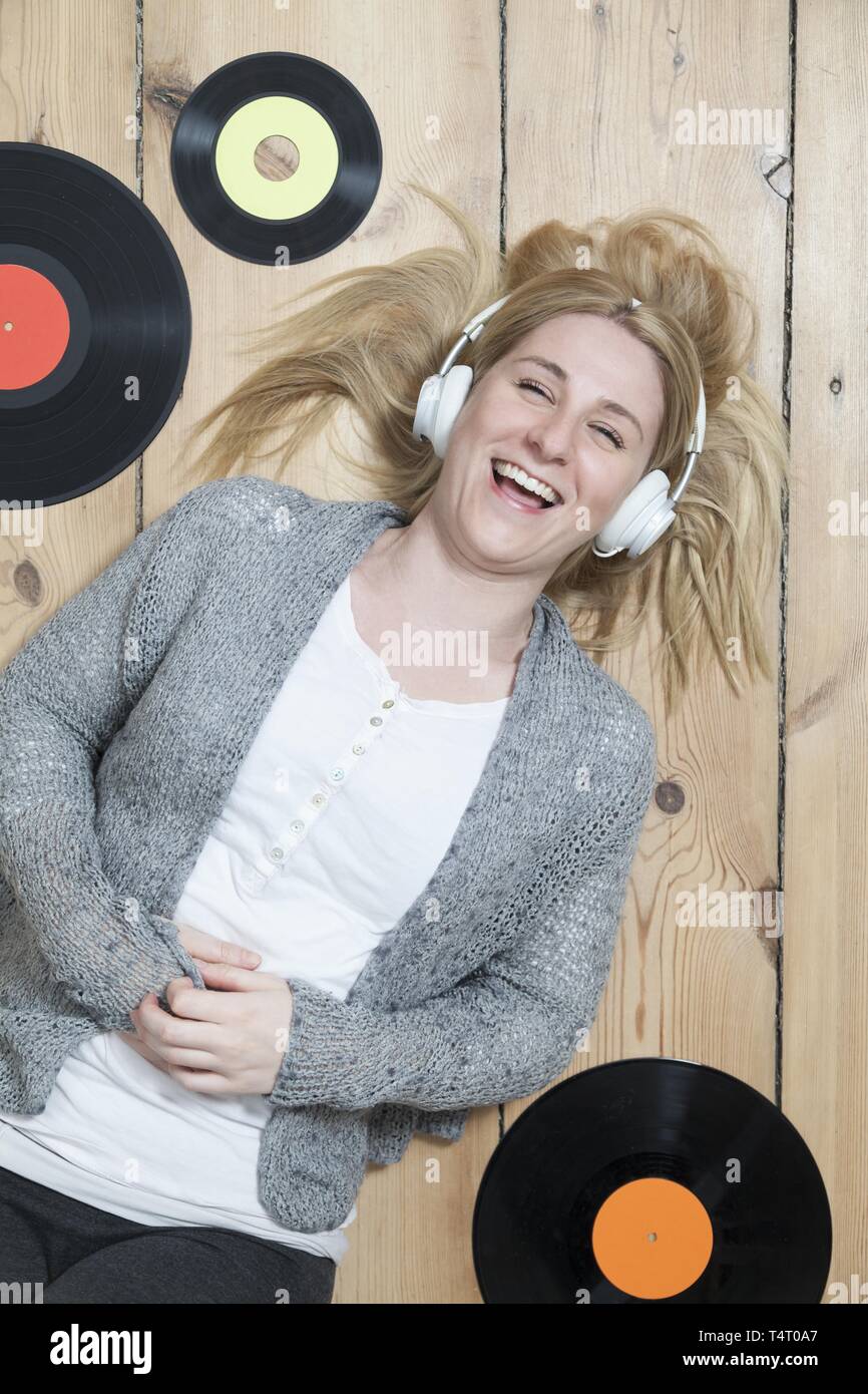 Junge blonde Frau liegend auf dem Holzboden, umgeben von Aufzeichnungen Stockfoto