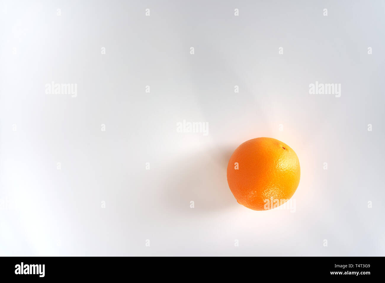Eine einzelne Orange auf einem weißen Tisch von oben fotografiert unter natürlichem Licht mit Schatten Stockfoto
