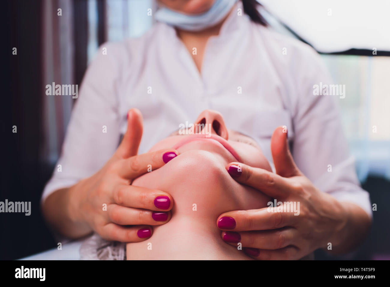 Kosmetiker macht eine bukkale Massage des Gesichts Die Muskeln des Patienten Stockfoto
