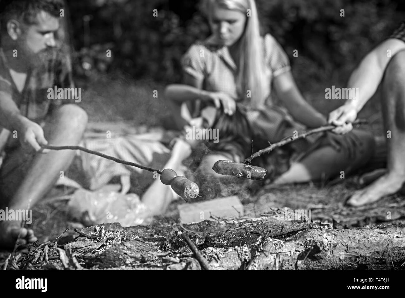 Übernachtung in Zelten im Sommer Picknick im Wald, Kochen im Freien. Zwei Paare von Lagerfeuer und braten Würstchen sitzen für Abendessen im Camp. Stockfoto