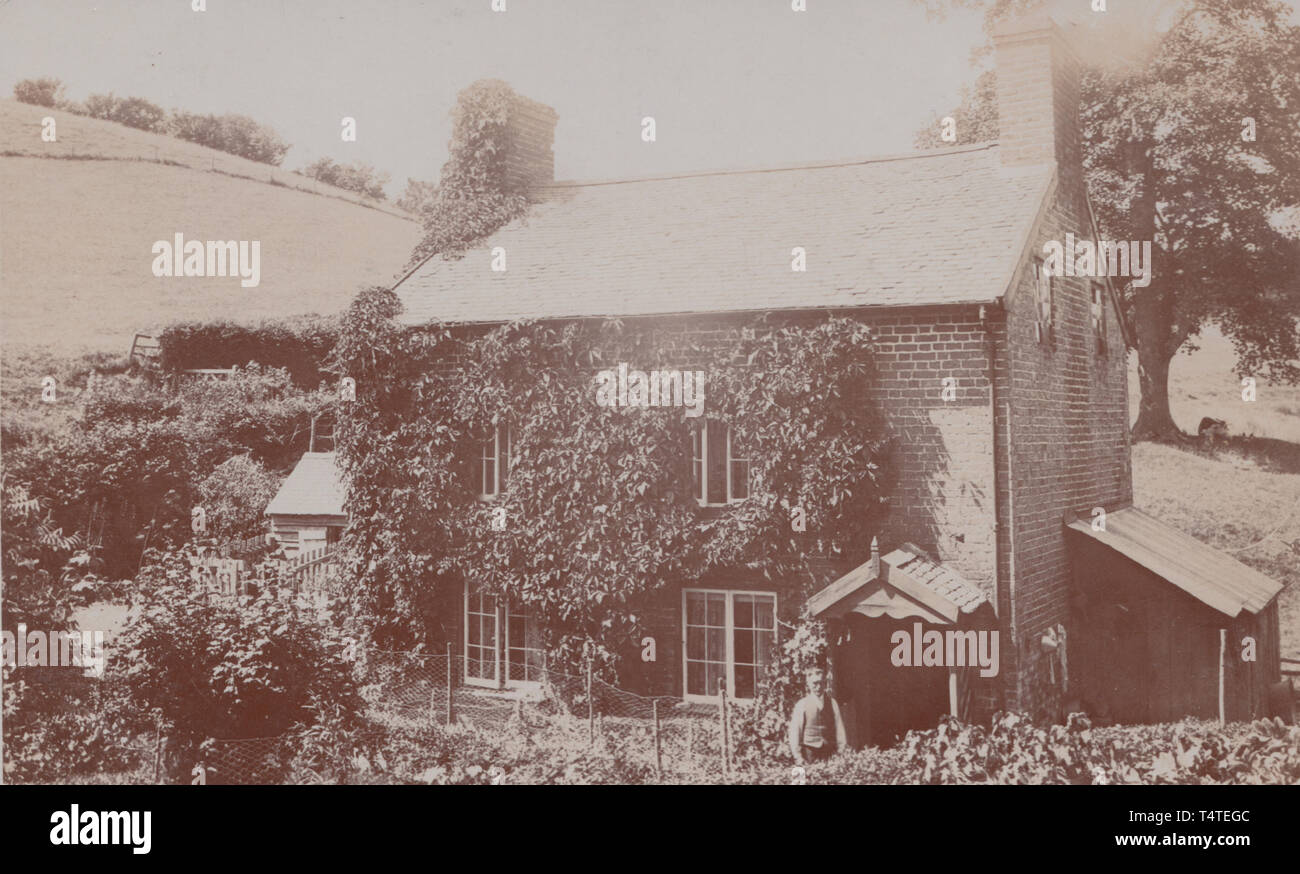 Jahrgang fotografische Postkarte zeigt einen historischen britischen Freistehendes Haus im Grünen. Insassen Stand Neben der vorderen Veranda. Stockfoto
