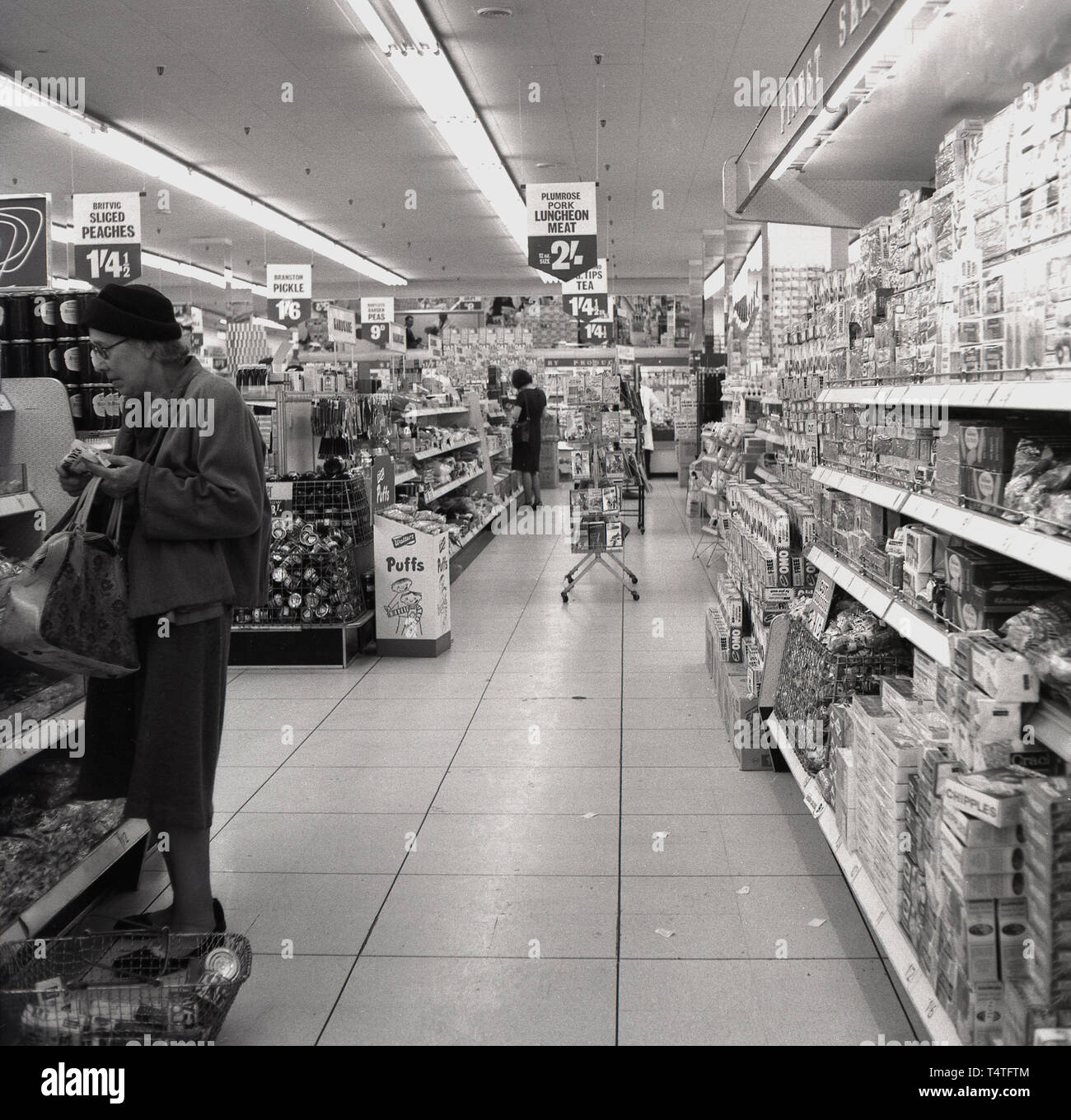 1960, historische, weiblichen Shopper in einem Gang in eine neue 'Feine Kost' Supermarkt, London, England. Feine Kost begann als Convenience Stores in den 1950er und in einer Supermarktkette in den folgenden zehn Jahren wuchs der Verkauf einer Vielzahl von Produkten einschließlich silced Pfirsiche und pork Luncheon Meat. Stockfoto