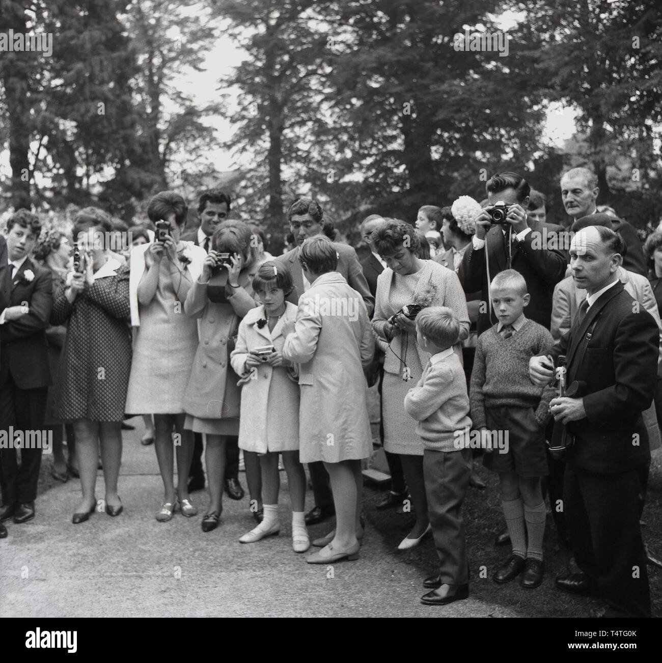 1960, historische, elegant gekleidete Gäste bei einer Hochzeit außerhalb Fotografieren mit Film und Video Kameras der Ära, England, UK. Stockfoto