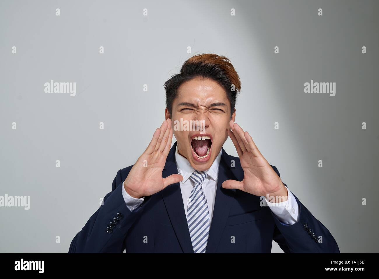 Junge asiatische Geschäftsmann schreien mit den Händen legte in seinen Mund, auf grauem Hintergrund Stockfoto