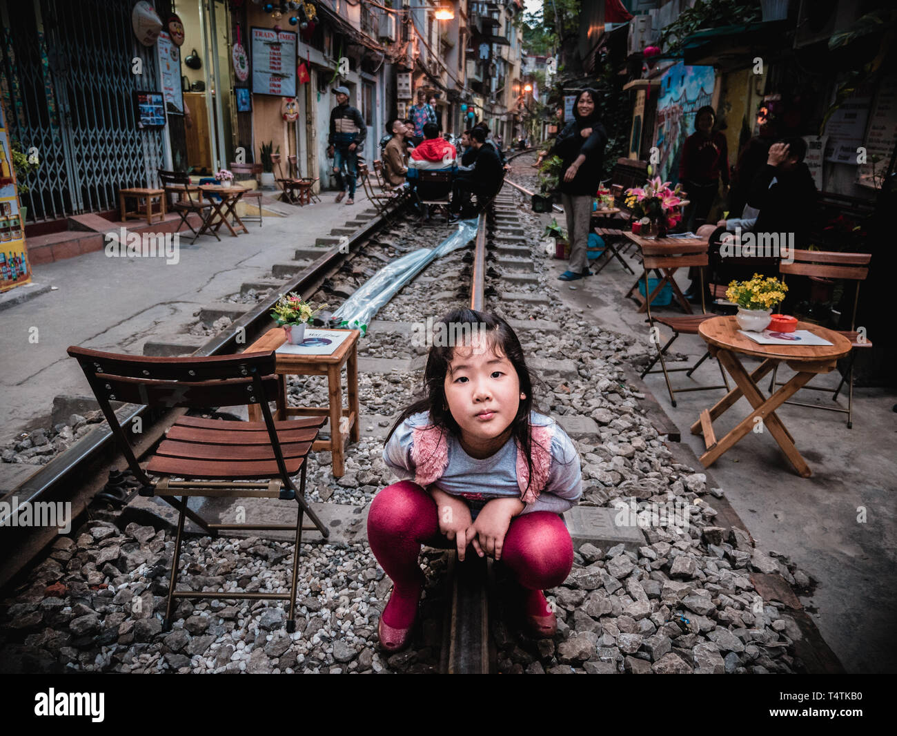 Neugierig vietnamesisches Mädchen hocken auf Schienen und sieht in die Kamera in Zug Straße der Stadt Hanoi, Vietnam Stockfoto