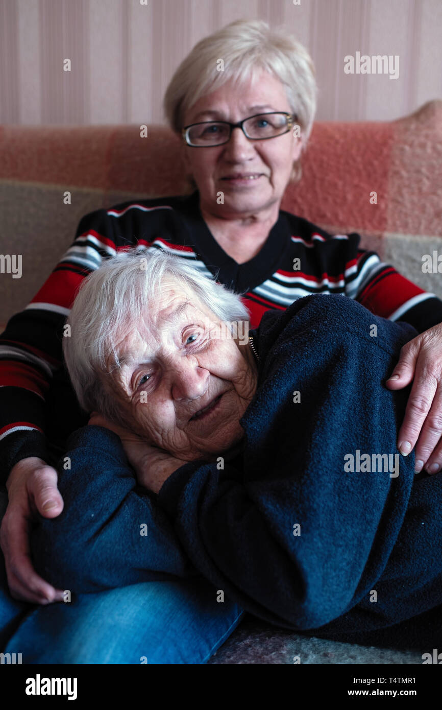 Alte Dame liegt auf Schoß ihrer erwachsenen Tochter. Stockfoto