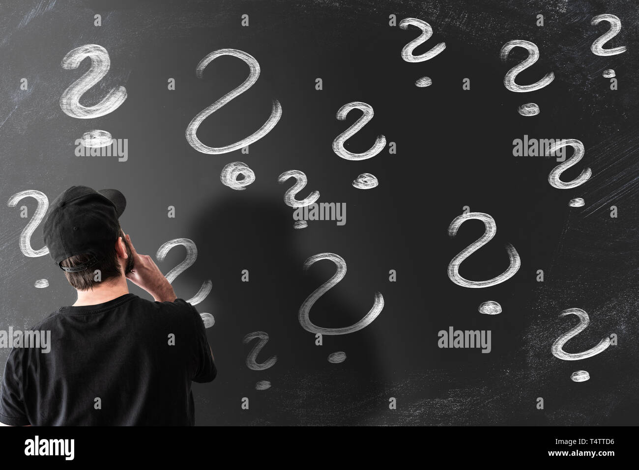 Ansicht der Rückseite des verwirrten Mann am Schwarzen Brett oder Blackboard mit Fragezeichen gefüllt suchen Stockfoto