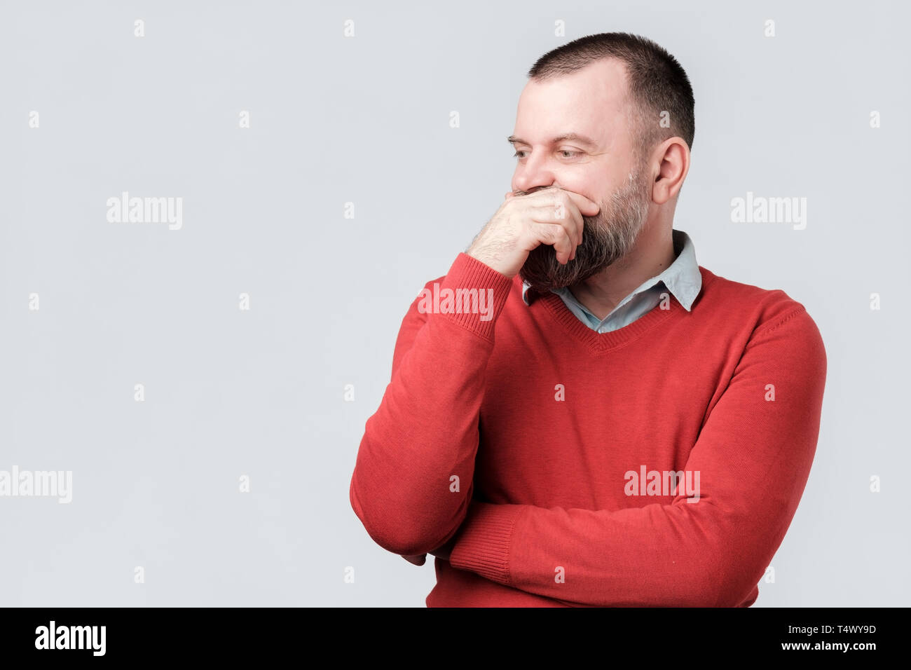 Reifer Mann im roten Pullover beiseite Denken und sein Kinn Reiben auf der Suche Stockfoto
