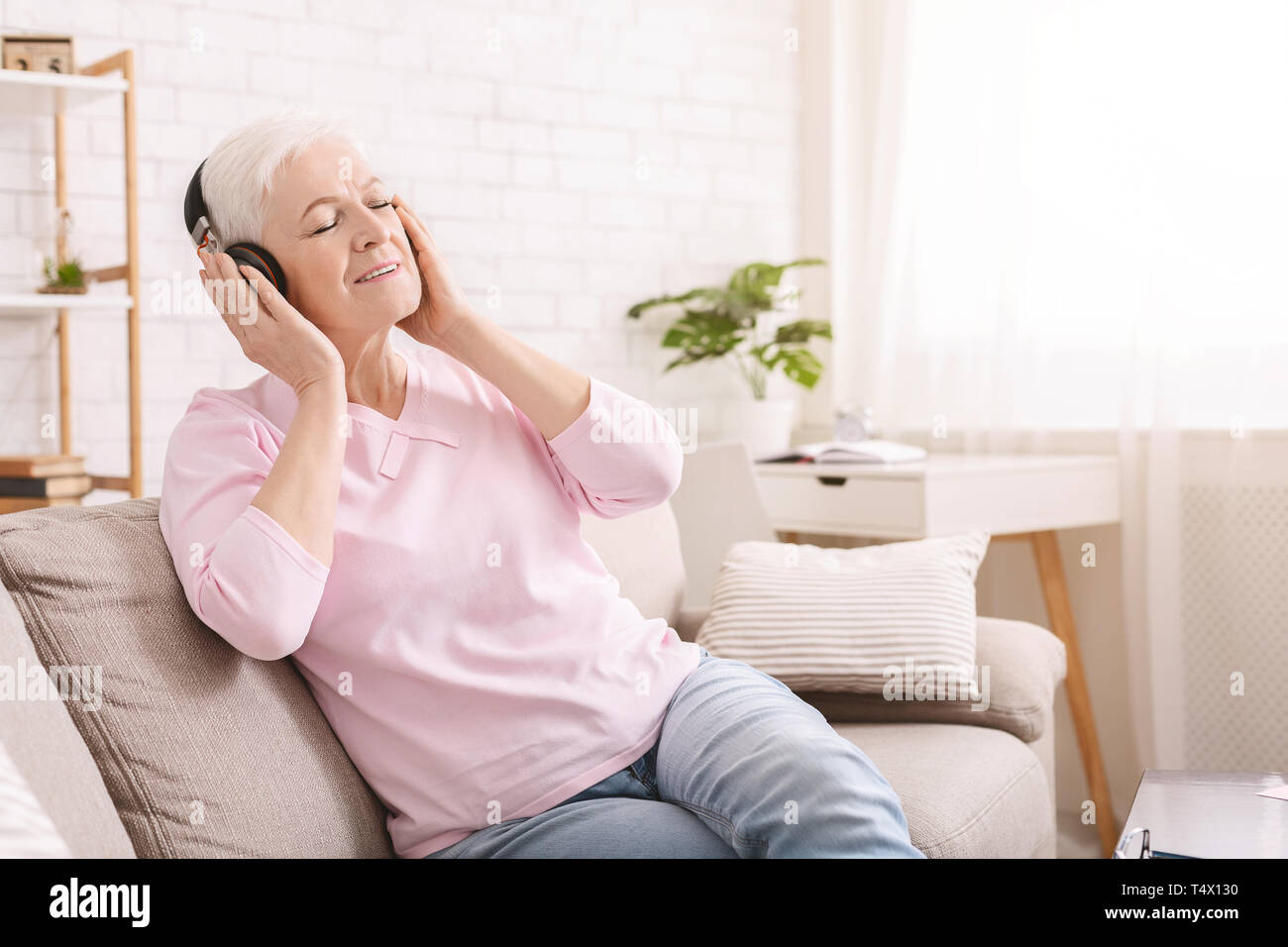 Ältere Frau genießen Hörbuch in Kopfhörer zu Hause Stockfoto