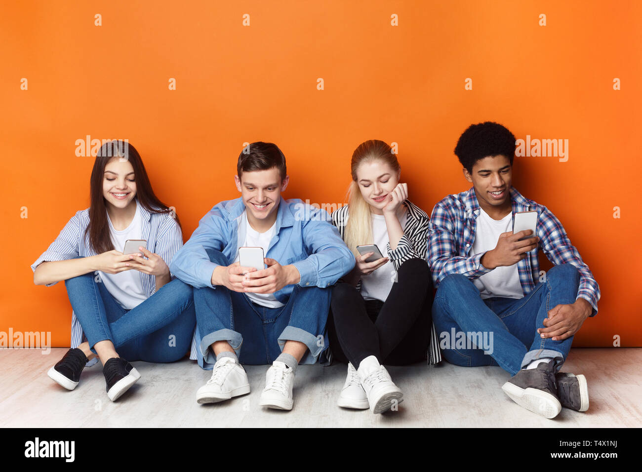 Gadget sucht. Jugendliche mit Smartphones, orange Wand Stockfoto