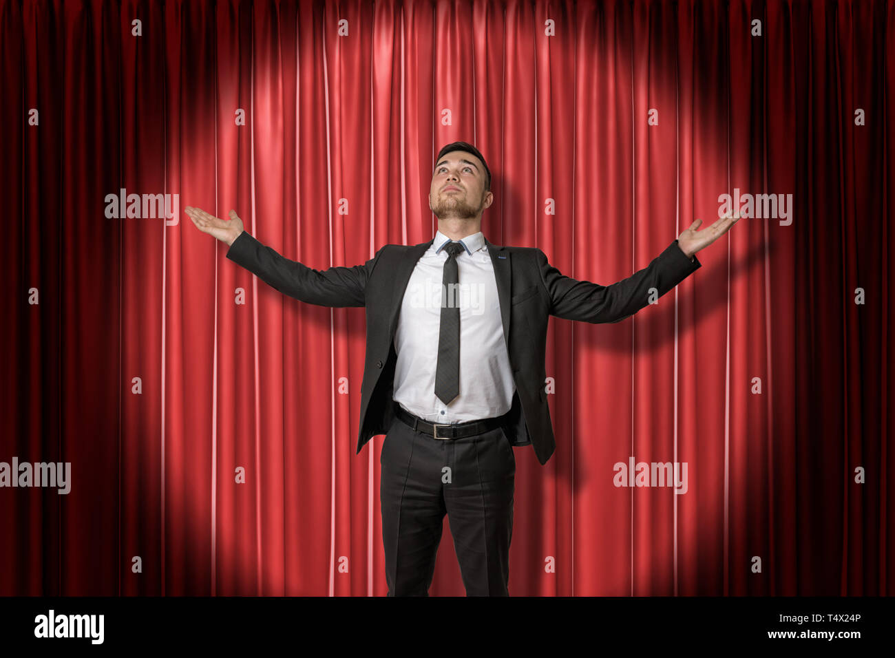 Glückliche junge Unternehmer stehen und sah mit Arme zur Seite ausbreiten von Spotlight beleuchtet, gegen roten Bühnenvorhang. Stockfoto