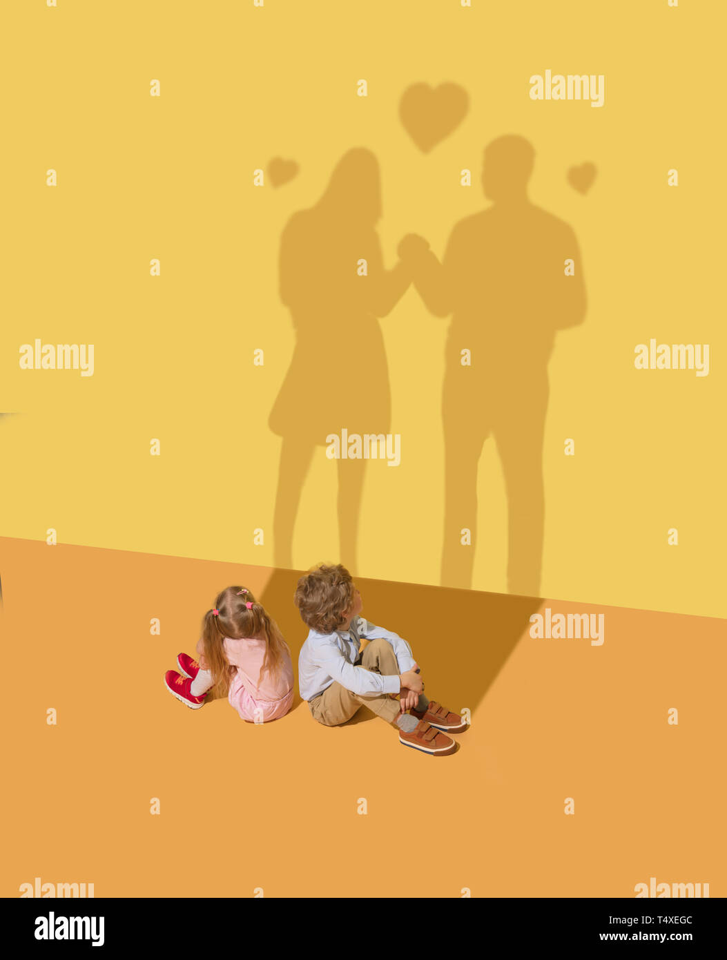 Neue Gefühle. Kindheit und Traum Konzept. Konzeptionelle Bild mit Kind und Schatten auf die gelbe studio Wand. Kleine Jungen und Mädchen ein Paar zu werden und haben romantische Beziehungen und Liebe. Stockfoto