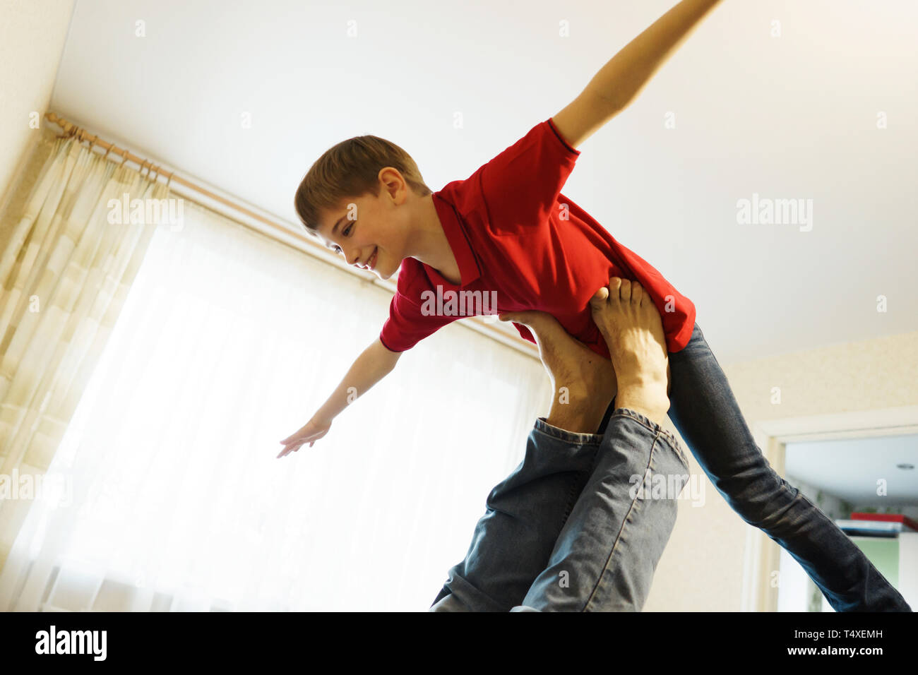 Der junge zeigt ein Flugzeug mit ausgestreckten Armen, an den Beinen seines Vaters unterstützt. Stockfoto