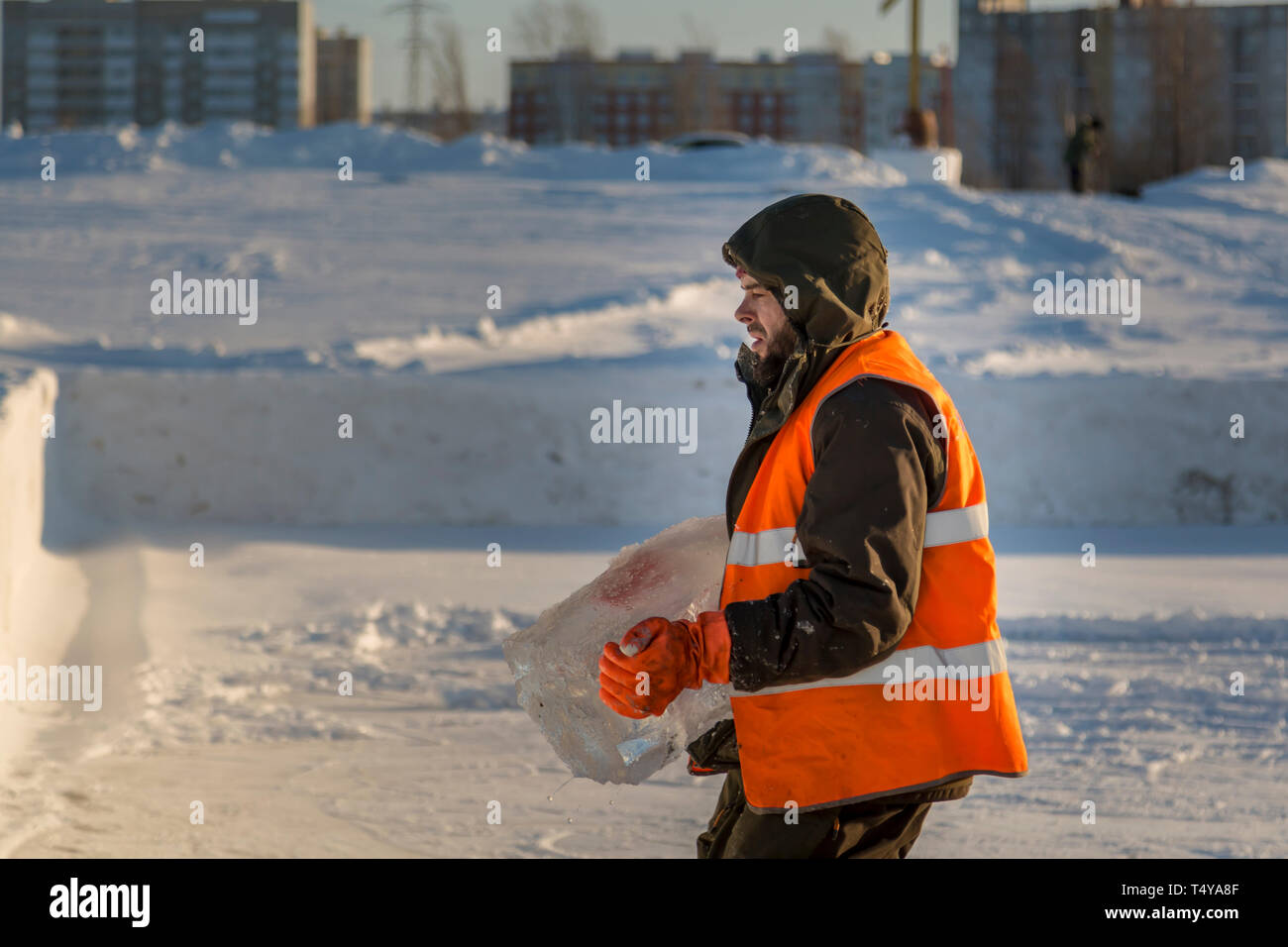 Ein Arbeiter in einem orangefarbenen Warnweste trägt einen Eisblock aus der Bohrung in der Hand. Stockfoto