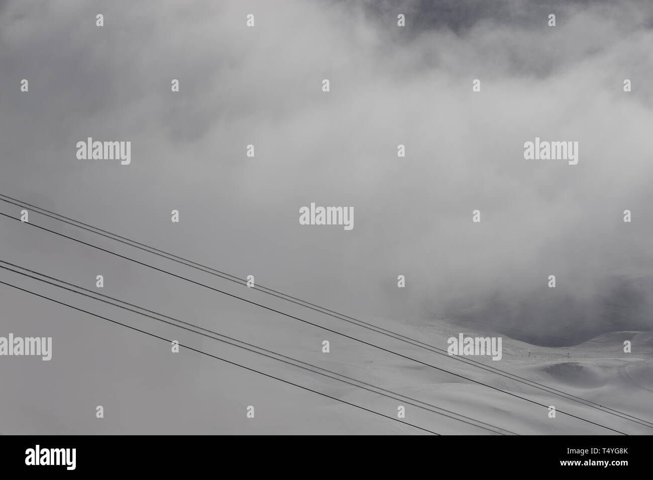 Zugspitze: Fahrt mit der Seilbahn über den Gletscher. Die Wolken verhüllen die Pisten. Im Vordergrund schräg die Seile der Seilbahn. Stockfoto