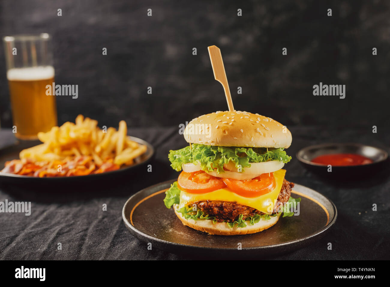 Fast food. Eine große Burger mit Rindfleisch und ein Glas Bier. Auf schwarzem Hintergrund Stockfoto