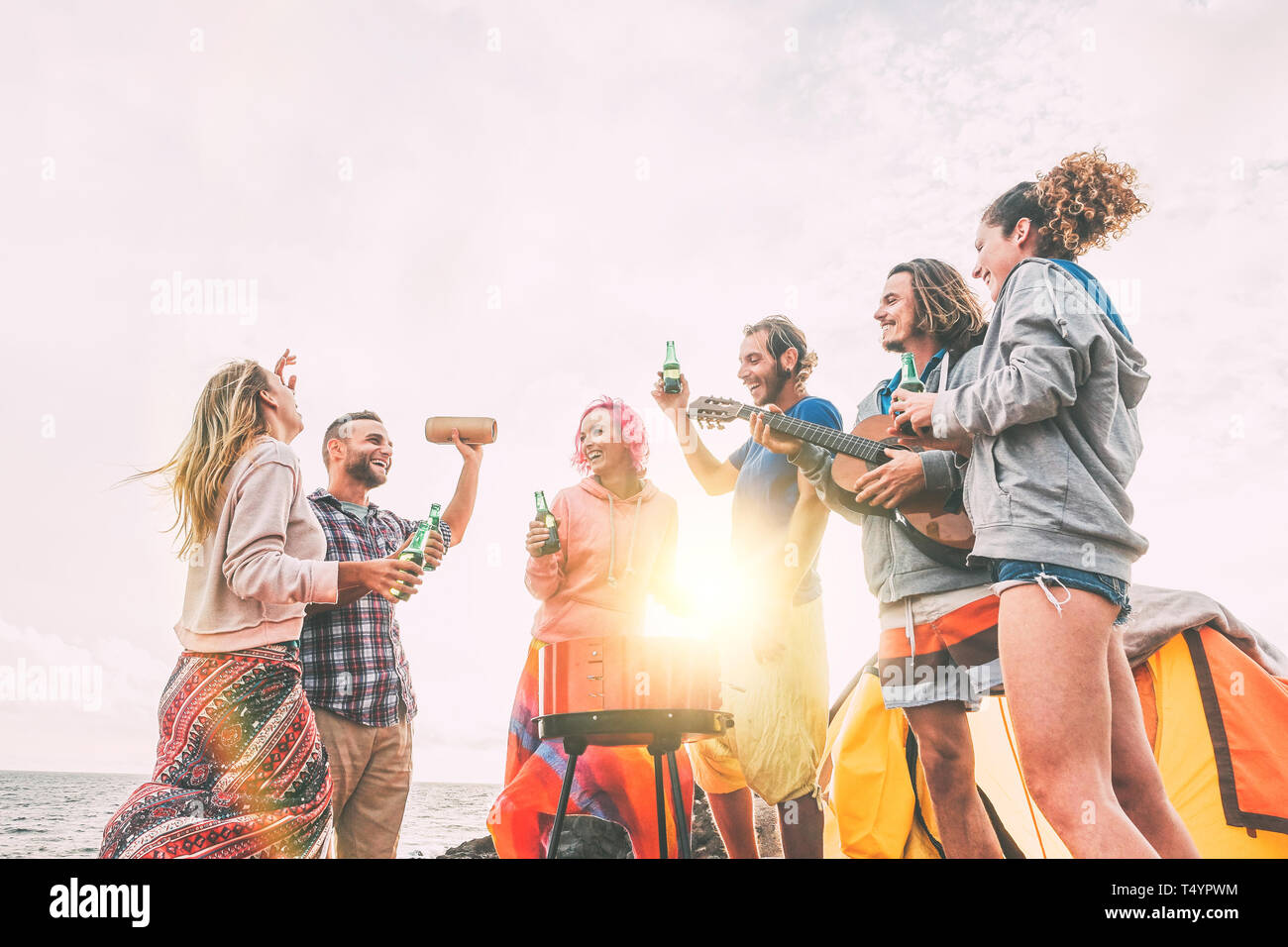 Eine Gruppe von Freunden mit Grill trinken Bier beim Camping am Strand - glückliche Menschen genießen Camp bbq Gitarre spielen und Musik hören Stockfoto