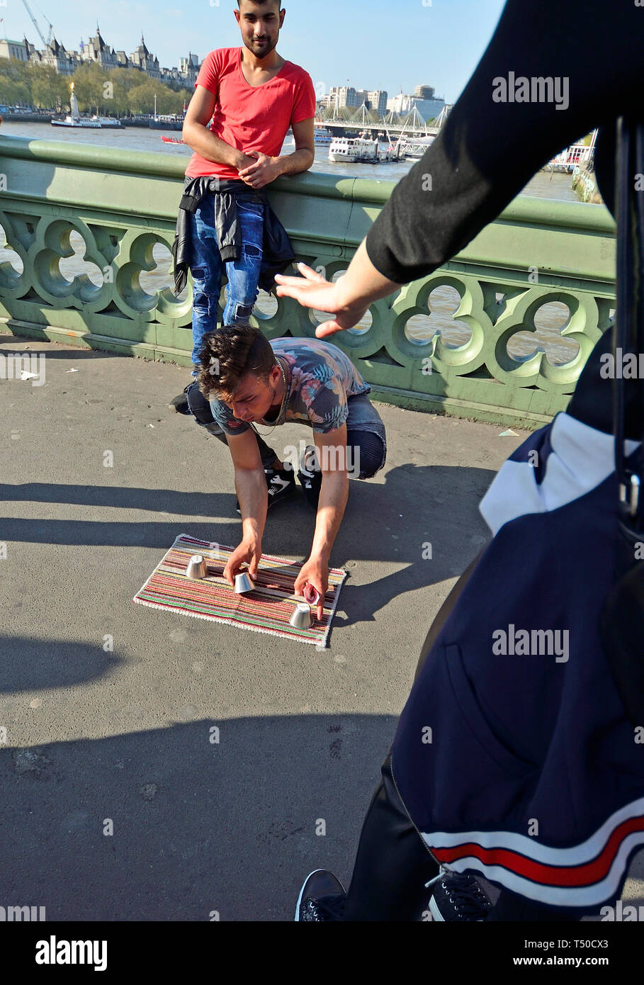 London, Großbritannien. 19. Apr 2019. Auf einer belebten Karfreitag Feiertag, den Bürgersteig auf die Westminster Bridge ist fast mehr als 10 illegale Spiele der 3 Tassen Trick oder Cup und Ball, entworfen, um Touristen ihr Geld durch Handlanger anscheinend gewinnen große Summen zu entlasten blockiert. Credit: PjrFoto/Alamy leben Nachrichten Stockfoto