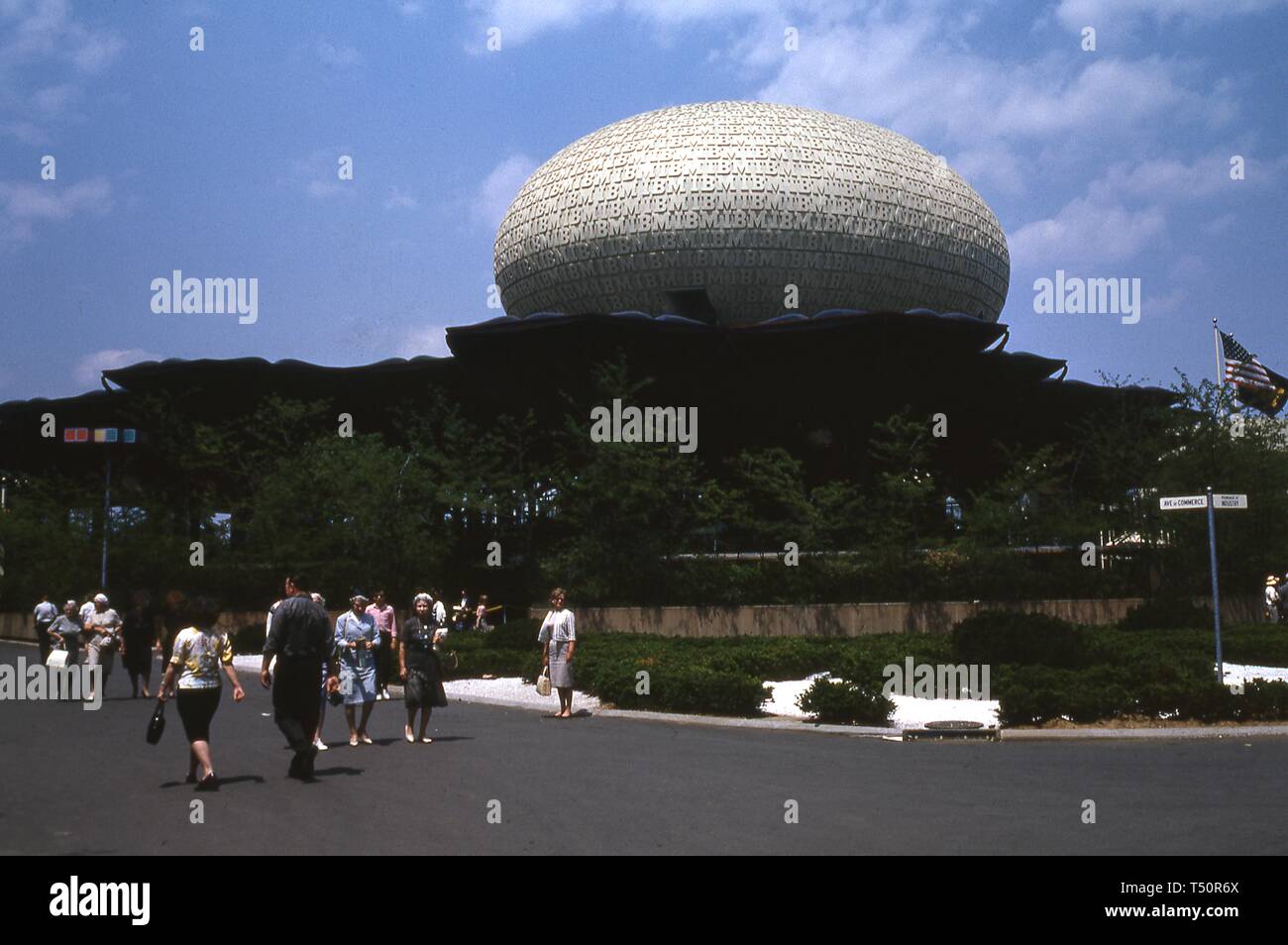 Eine Frau steht in voller Länge zu sehen, auf einer belebten Fußgängerzone vor der IBM Pavillon posiert, an einem sonnigen Tag, in New York World's Fair, Flushing Meadows Park, Queens, New York, Juni 1964. () Stockfoto