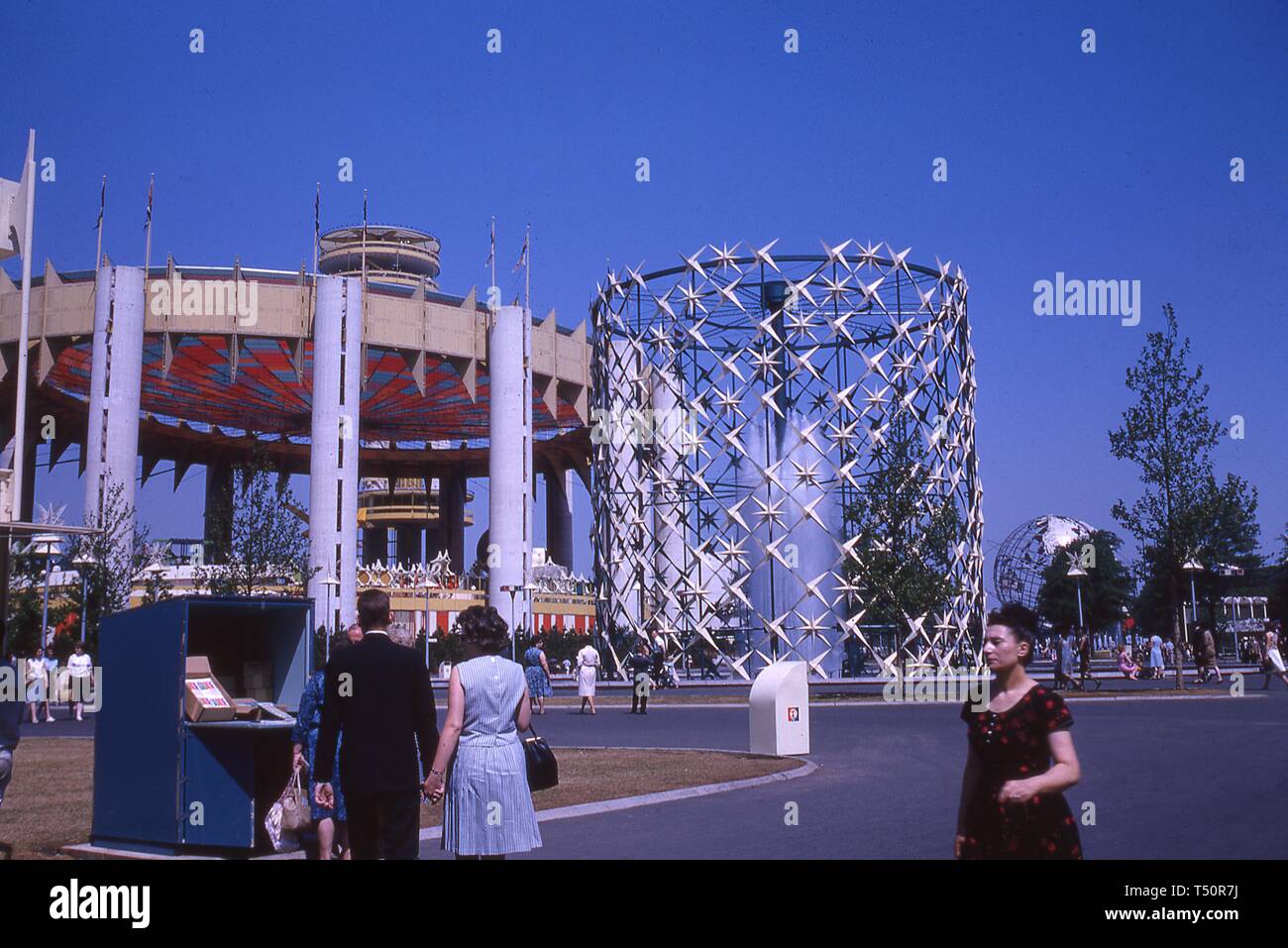 Mehrere Personen Ansatz einen Stand mit Flyer, an einem sonnigen Tag, in der Nähe von einem Brunnen, der Staat New York Pavillon und die Unisphere, in New York World's Fair, Flushing Meadows Park, Queens, New York, Juni 1964. () Stockfoto