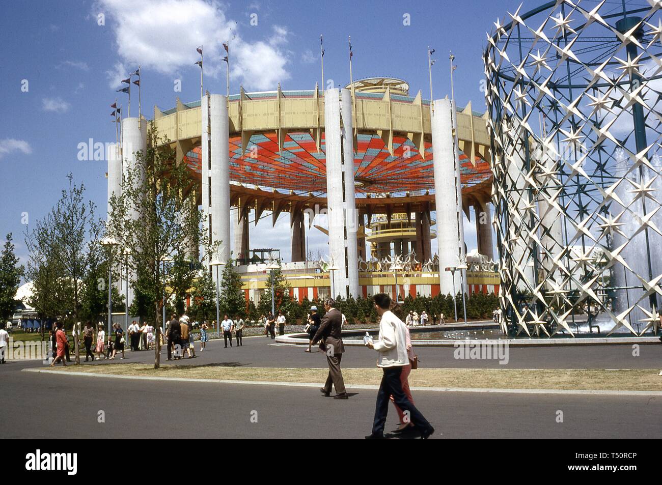 Menschen laufen auf einem gepflasterten Bereich, an einem sonnigen Tag, in der Nähe der astralen Brunnen und das New York State Pavilion, 1964 in New York World's Fair, Flushing Meadows Park, Queens, New York, Mai, 1964. () Stockfoto