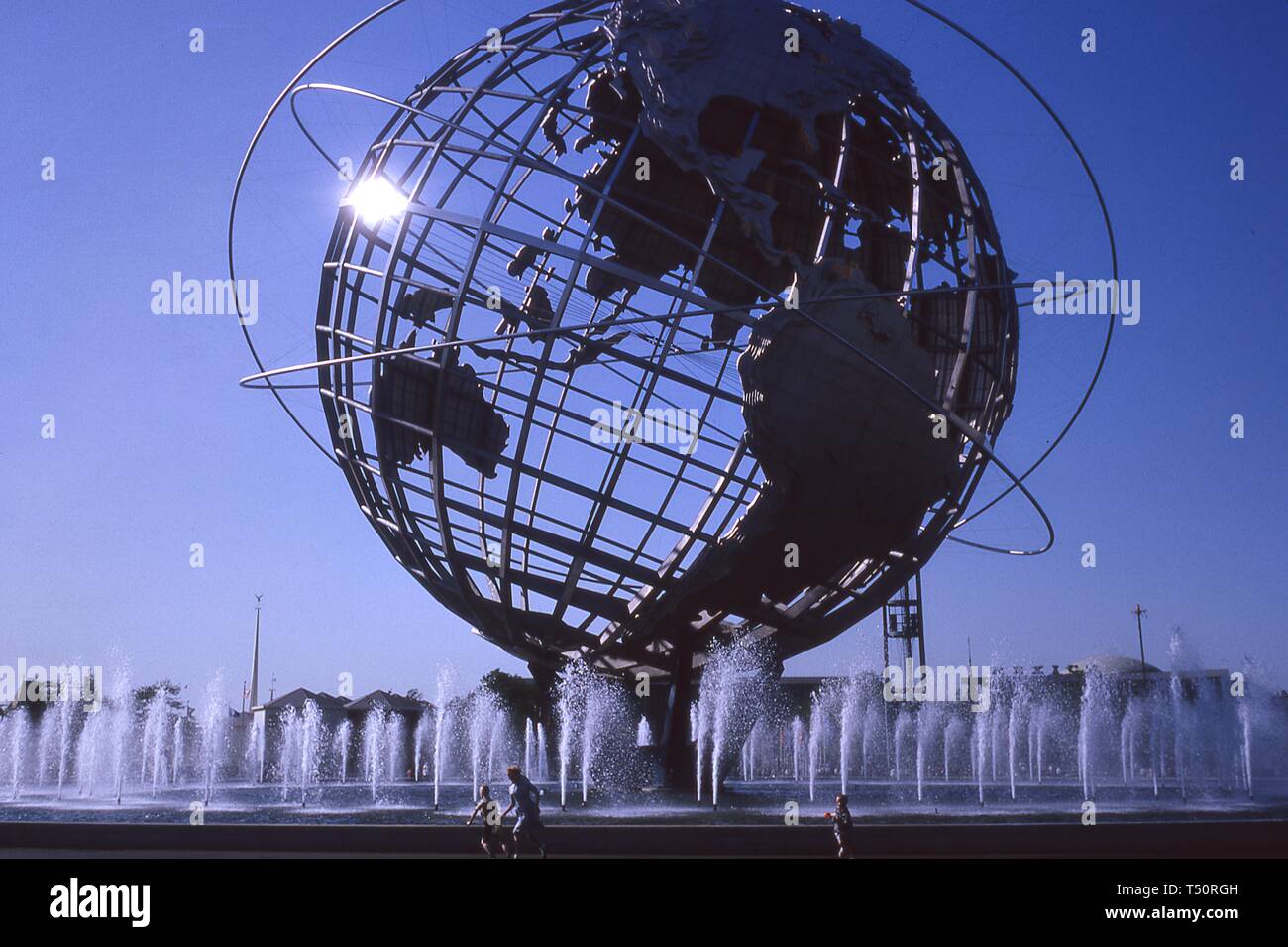 Einige Leute gehen in der Nähe der Brunnen der Kontinente und zentralen Unisphere, an einem sonnigen Tag, mit dem Mexiko Pavillon im Hintergrund, 1964 in New York World's Fair, Flushing Meadows Park, Queens, New York, Mai, 1964. () Stockfoto