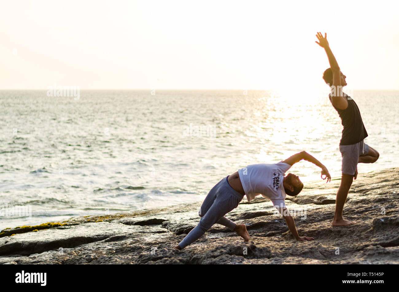 Zwei Freunde Üben Yoga am Rand des Ozeans bei Sonnenuntergang, Yoga oder Meditation Konzept Stockfoto